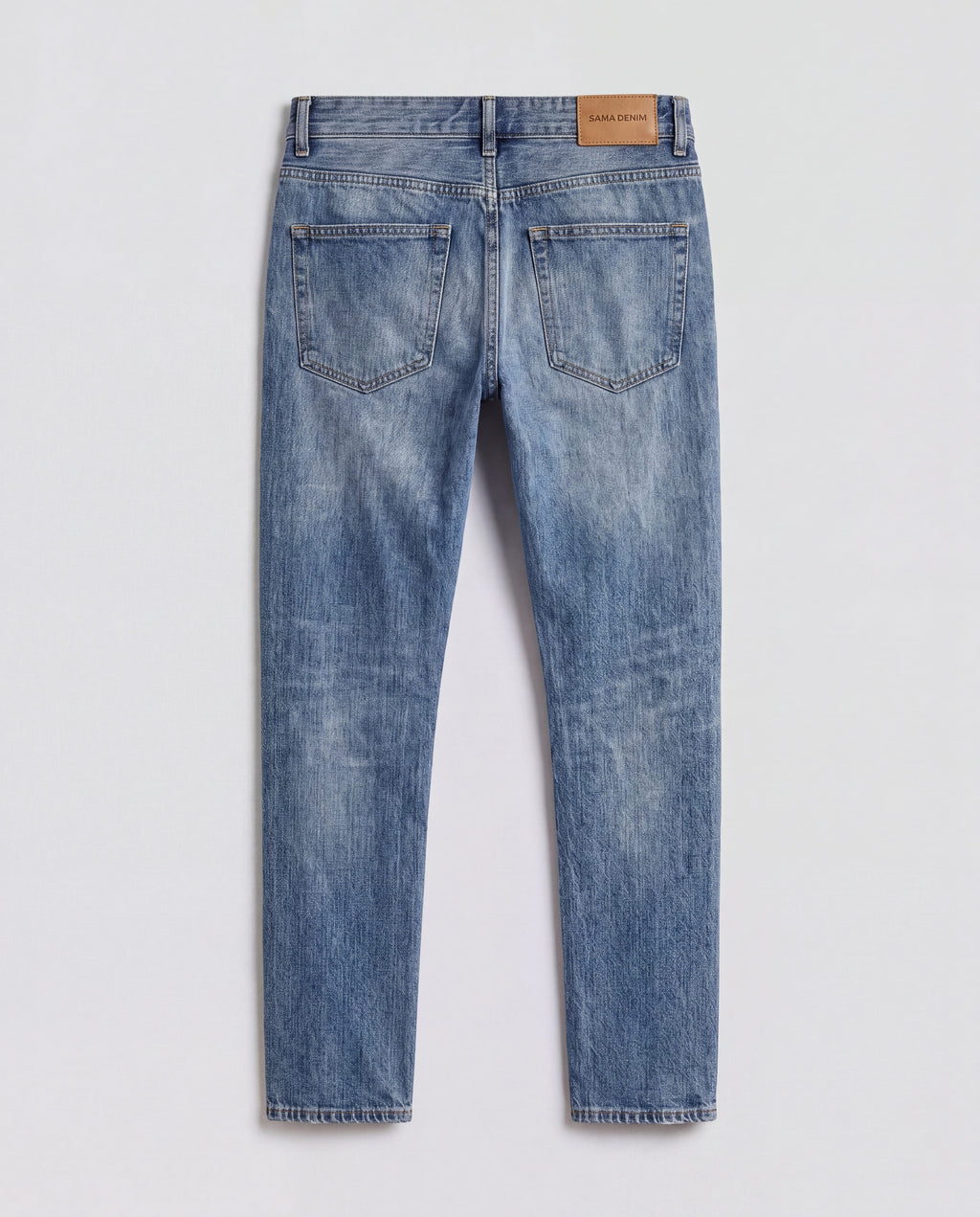 Back flat lay view of Sama Denim men's light wash slim fit jeans with signature leather patch