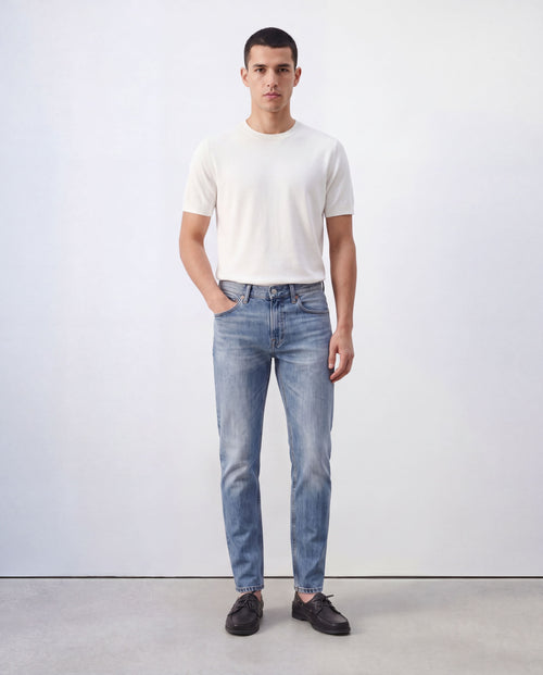 Model wearing Sama Denim men's light wash slim fit jeans with white t-shirt in minimalist studio